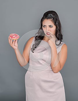 Plus size woman looking on donut with doubt. Overweight concept