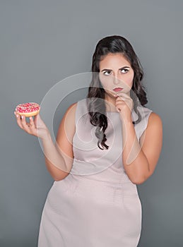 Plus size woman thinking about eating donut. Overweight concept