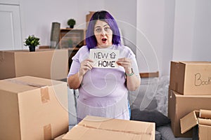 Plus size woman wit purple hair moving to a new home holding banner in shock face, looking skeptical and sarcastic, surprised with