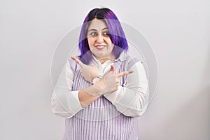 Plus size woman wit purple hair standing over white background pointing to both sides with fingers, different direction disagree
