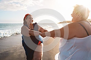 Plus size women dancing on the beach having fun during summer vacation - Curvy female laughing together - Overweight body and