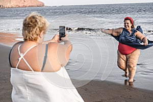 Plus size women friends having fun taking photos on the beach - Focus on right woman