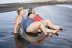 Plus size women sitting on the beach having fun during summer vacation - Focus on faces