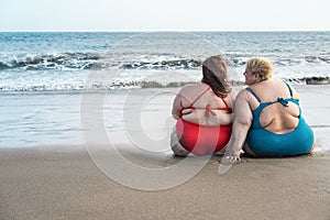 Plus size women sitting on the beach having fun during summer vacation - Rear view of curvy female laughing together - Overweight