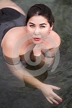 Plus size young woman with big breast in black swimsuit lying in outdoor pool at balneotherapy spa photo