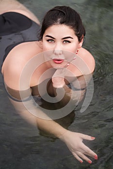 Plus size young woman with big breast in black swimsuit lying in outdoor pool at balneotherapy spa