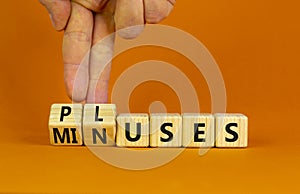 Pluses and minuses symbol. Businessman turns wooden cubes and changes the word `minuses` to `pluses`. Beautiful orange table,