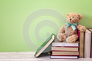 Plush bear with stack of book on a green background. Copy space.