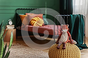 Plush fox on yellow pouf on the floor of colorful teenager`s room