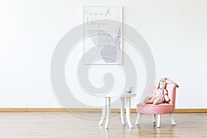 Plush toy on pink chair at table in white girl`s room interior w