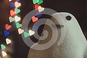 A plush white penguin looks at the camera against a background of colorful bokeh in the shape of hearts.