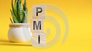 pmi concept with wooden blocks on table, yellow background