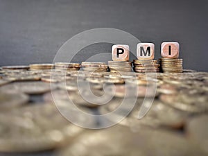 PMI text on wooden cubes with coin stacks background. Business concept.