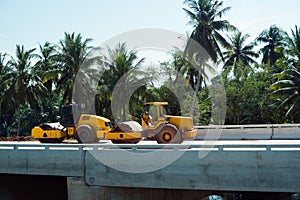 Pneumatic roller compactor at asphalt pavement works for road repairing on a construction site with a palm trees on