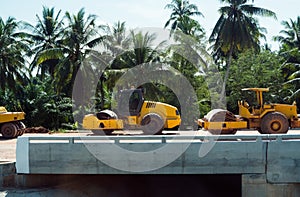 Pneumatic roller compactor at asphalt pavement works for road repairing on a construction site with a palm trees on