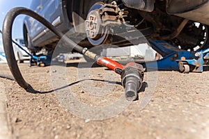 Pneumatic wrench tool on the asphalt and a car jack for lift up the body and changing the tire. Car without wheel