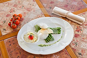 Poached egg with grilled asparagus sprouts, served on a white oval plate under a cheese crust with mashed potatoes and tomatoes.