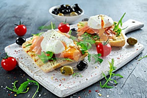 Poached egg on grilled toast with smoked salmon, rucola, olives and vegetables on white board. healthy breakfast