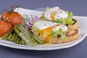 Poached egg on a piece of bread with fried green beans, tomato and arugula on a plate
