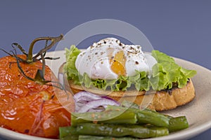 Poached egg on a piece of bread with fried green beans, tomato and arugula on a plate