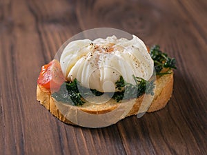 Poached egg with a slice of tomato and roasted herbs on a piece of bread on a wooden table.