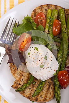 Poached egg on toasted bread with asparagus, tomatoes and greens