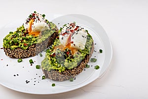 Poached eggs with avocado guacomole on brown bread with sesame seeds. Healthy breakfast on a white background.