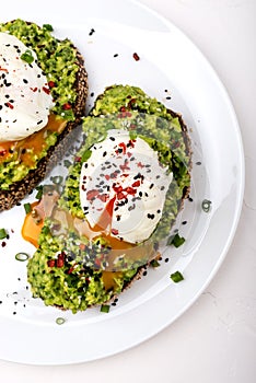 Poached eggs with avocado guacomole on brown bread with sesame seeds. Healthy breakfast on a white background.