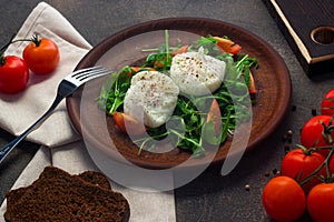 Poached eggs on lettuce and arugula, on a clay plate. Dark background
