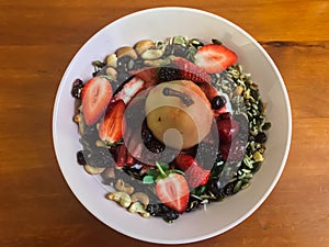 Poached pear and fresh berries granola breakfast cereal served in white bowl set on wooden table