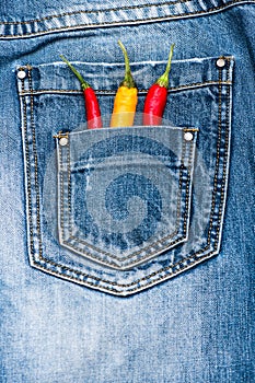 Pocket of jeans staffed with red and yellow chilly peppers, denim background. Peppers in back pocket of blue jeans