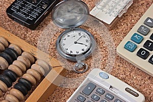 pocket watch, a calculator, a wooden abacus on a cork board