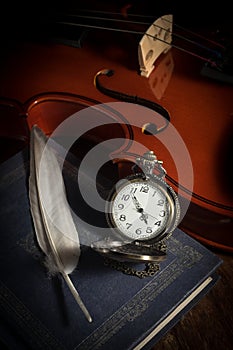 Pocket watch with feather on book and violin.