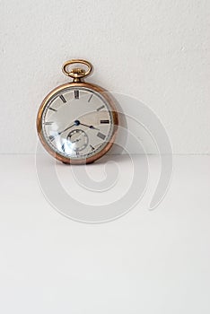 Pocket watch in gold on white paper and supported on the wall