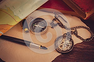 Pocket watch with old books and pen with paper map on the table.