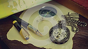 Pocket watch with old books and pen with paper map on the table by the window.