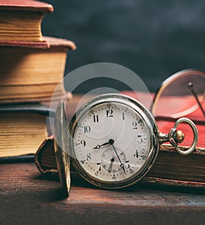 Pocket watch and old books on a wooden office desk background