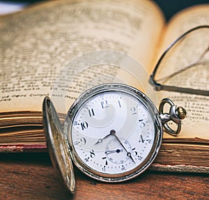 Pocket watch and old books on a wooden office desk background