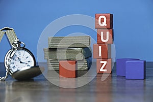 A pocket watch, stack of book and red wooden cube written with QUIZ on a table