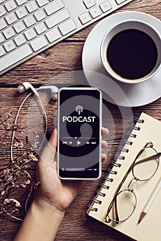 Podcast audio content concept. podcast application on mobile smartphone screen on wooden table with coffee cup, earphones, glasses