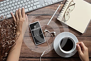 Podcast audio content concept. podcast application on mobile smartphone screen on wooden table with coffee cup, earphones, glasses