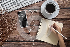 Podcast audio content concept. podcast application on mobile smartphone screen on wooden table with coffee cup, earphones, glasses