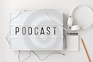 Podcast concept with headphones, notepad on white background, flat lay