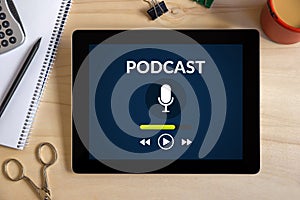 Podcast concept on tablet screen with office objects on wooden d