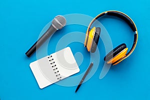 Podcast record with notebook, microphone and headphones on blue background top view space for text