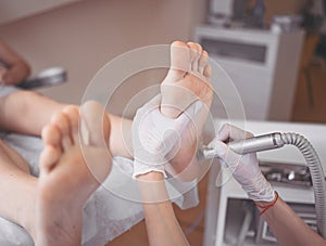 Podiatrist using grinding equipment and making procedure polish for feet pedicure. Podology beautician in white gloves