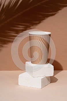 Podium made of natural stone with the shadow of tropical leaves in the background, paper cups. Beautiful background from