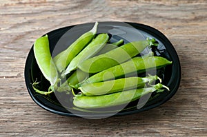 Pods of green peas in plate on wooden background