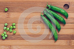 Pods of green peas on a wooden chopping Board top view. Space for text.