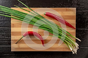 Pods of red hot chili peppers, green onion stalks and sharp metal knife on wooden cutting board. Spicy cayenne pepper